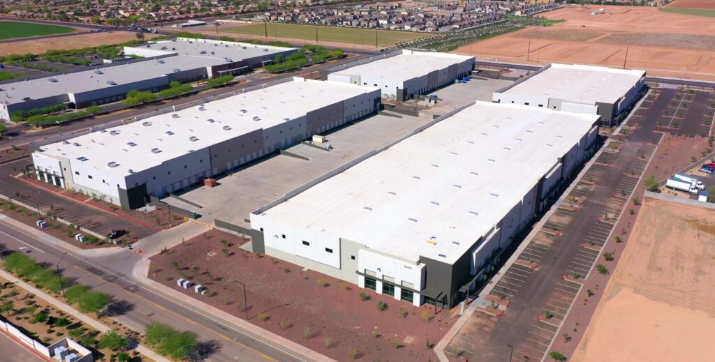 Aerial view of large, newly constructed warehouse buildings in an industrial park surrounded by parking lots and roads.