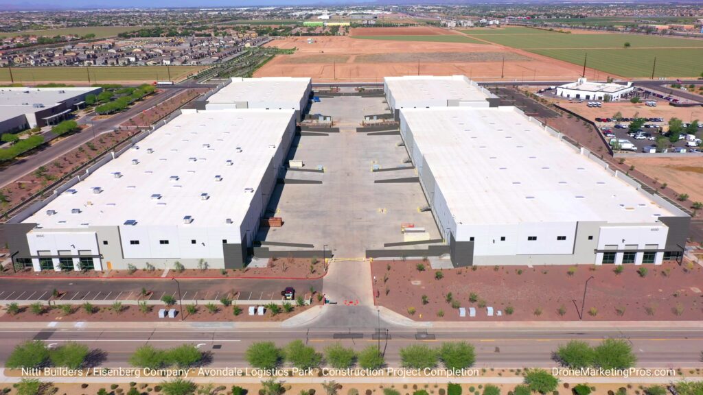 Aerial view of two large, identical warehouse buildings with a shared central driveway, surrounded by roads, parking areas, and landscaped grounds.