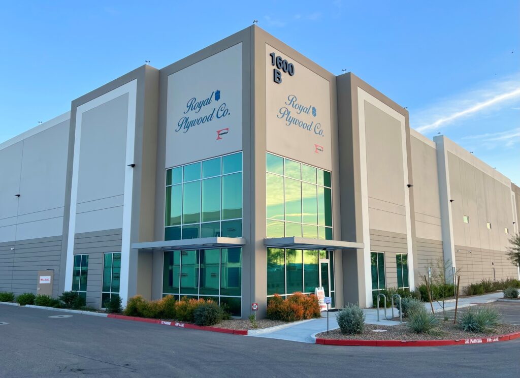 A modern industrial building with "Royal Plywood Co." signage and large reflective windows, located at 1600 E, surrounded by landscaping and a paved driveway.