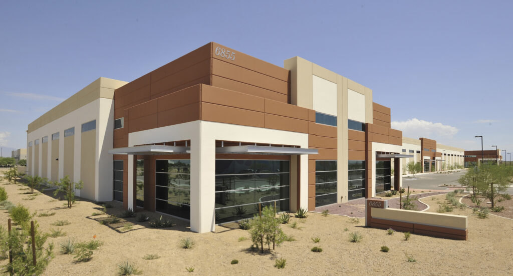 Modern, tan and brown commercial building with large windows, surrounded by desert landscaping and a clear sky. The building number 6855 is visible.